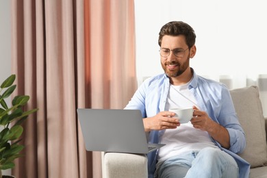 Photo of Man with cup of drink using laptop at home