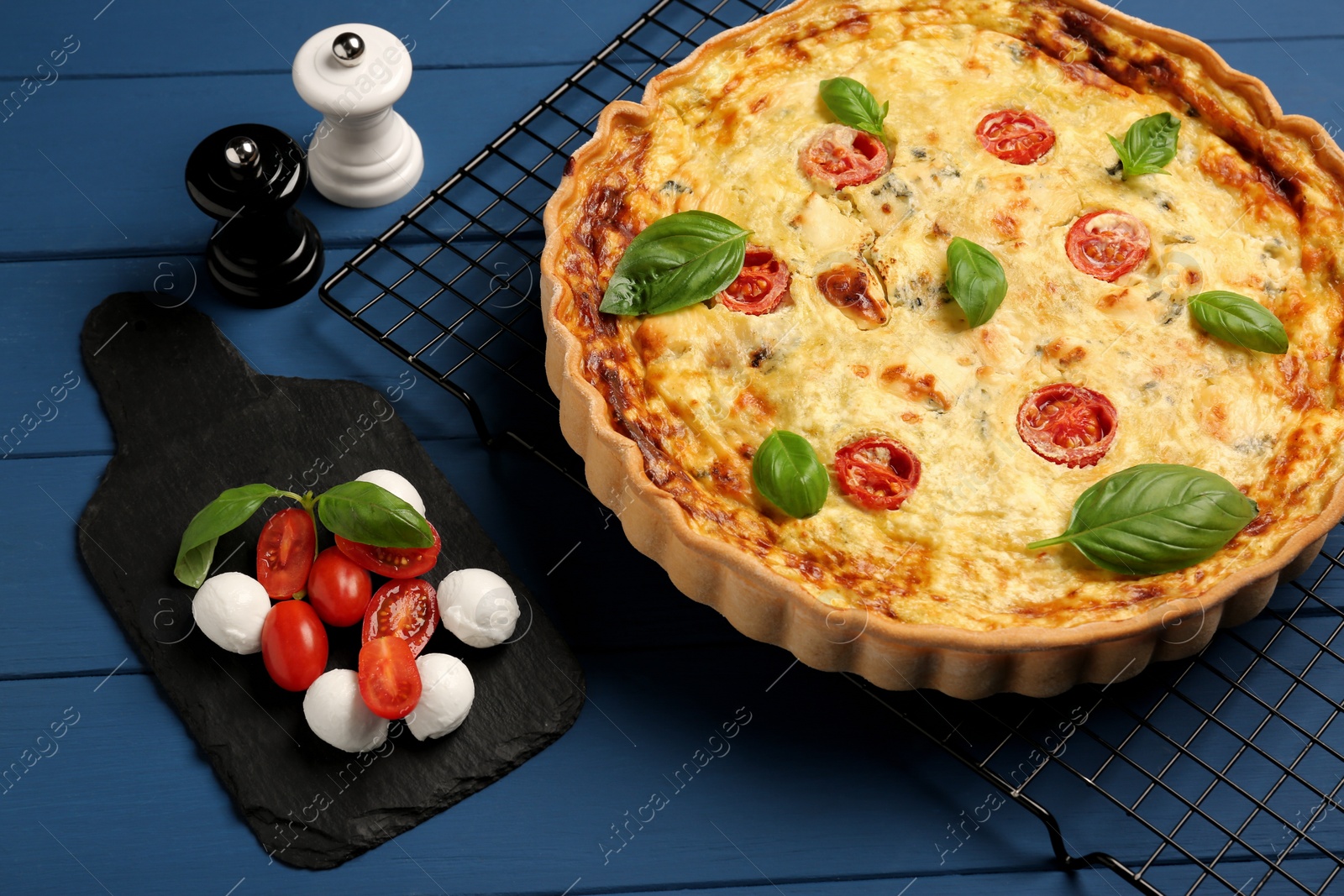 Photo of Delicious quiche with mozzarella cheese, tomatoes and basil on blue wooden table