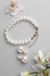 Photo of Elegant pearl earrings, bracelet and orchid flowers on white background, flat lay