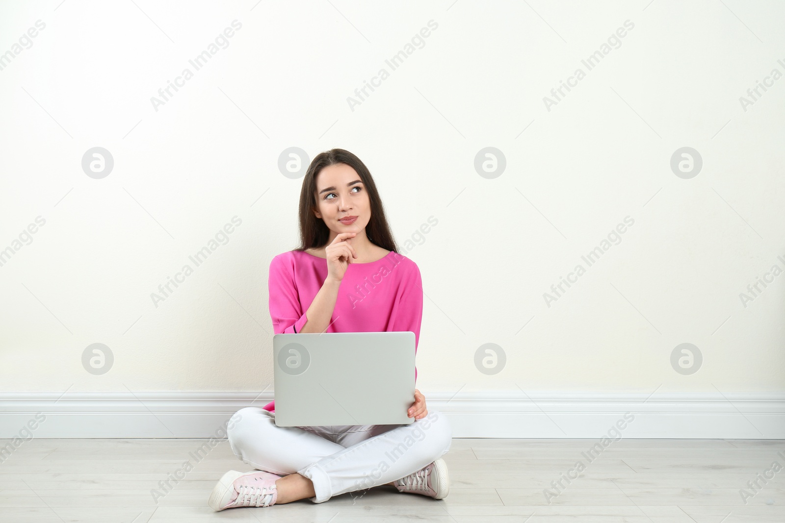 Photo of Young woman with laptop sitting on floor near light wall indoors. Space for text