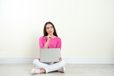 Photo of Young woman with laptop sitting on floor near light wall indoors. Space for text