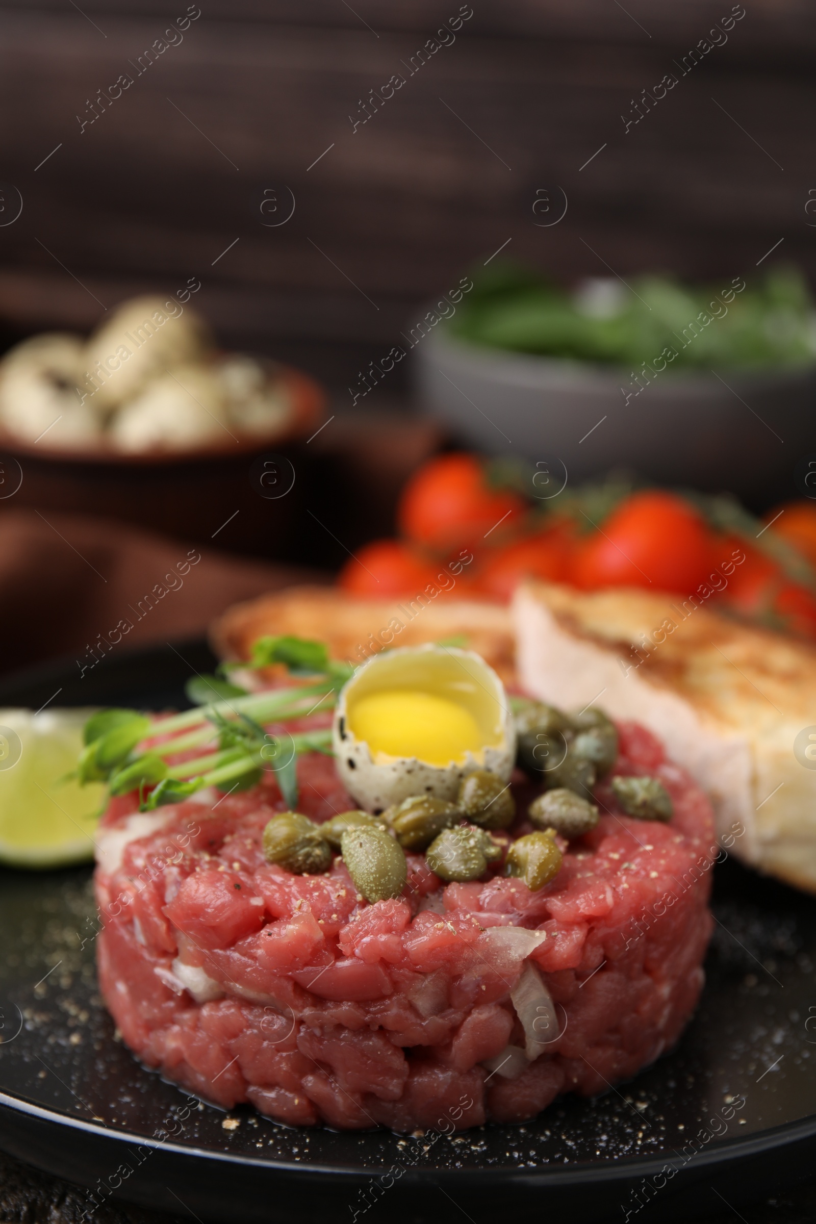 Photo of Tasty beef steak tartare served with quail egg and other accompaniments on black plate, closeup