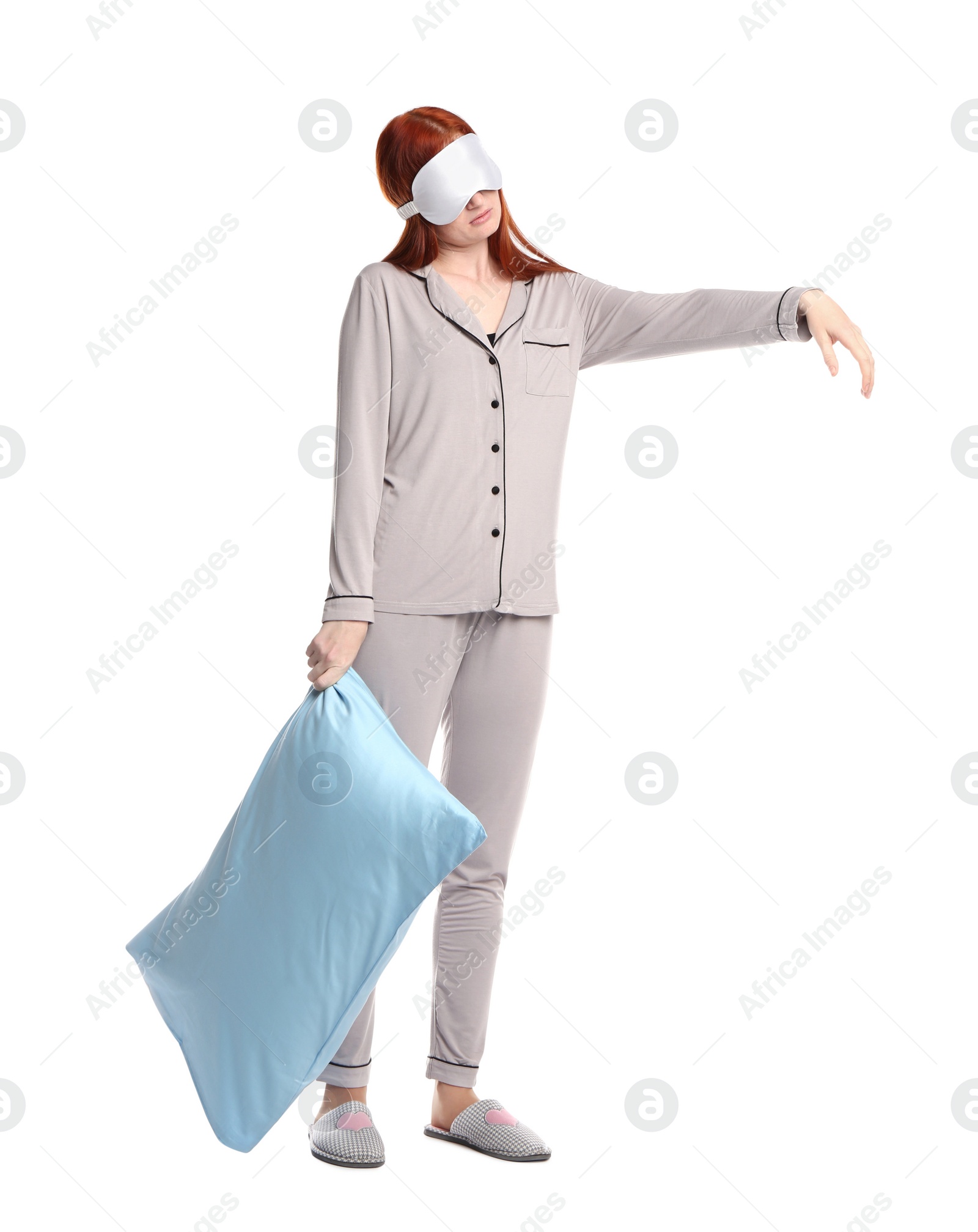 Photo of Young woman wearing pajamas and slippers with pillow in sleepwalking state on white background