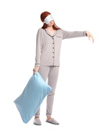 Photo of Young woman wearing pajamas and slippers with pillow in sleepwalking state on white background
