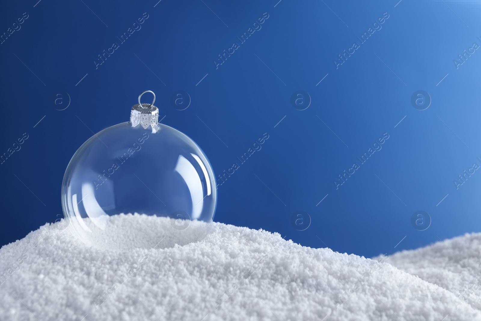 Photo of Transparent Christmas ball on snow against blue background, space for text