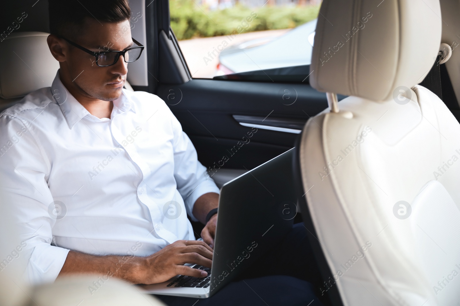 Photo of Handsome man working with laptop on backseat of modern car