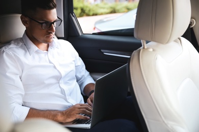 Photo of Handsome man working with laptop on backseat of modern car