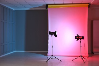 Photo of Photo background in neon lights and professional lighting equipment inside modern studio, space for text