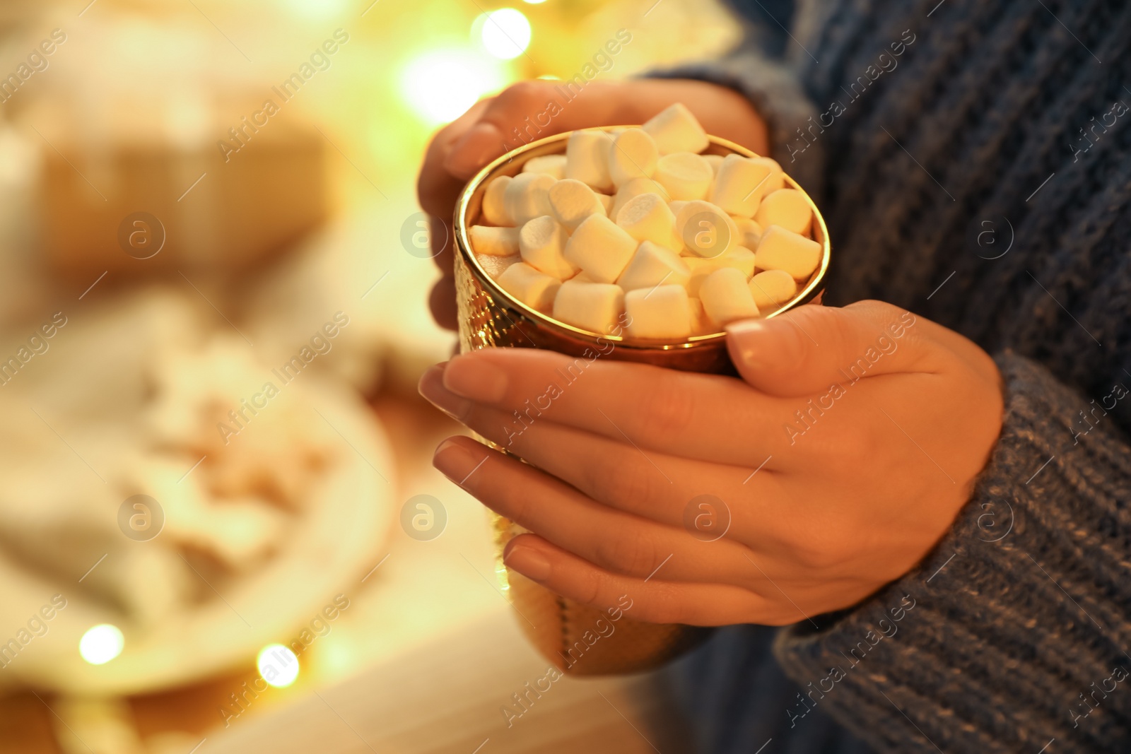 Photo of Woman holding cup of hot drink with marshmallows indoors, closeup. Magic Christmas atmosphere