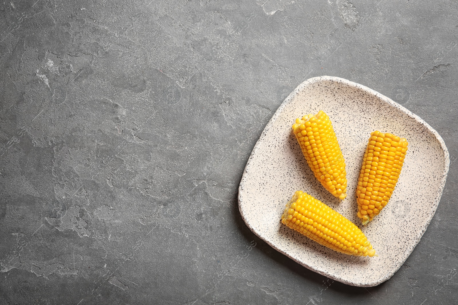 Photo of Plate with corn cobs on grey background, top view. Space for text