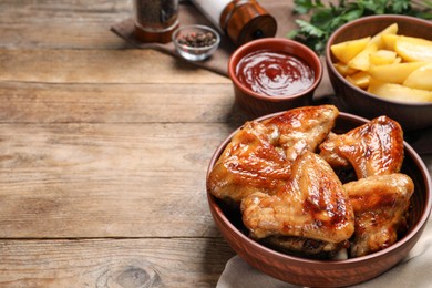 Photo of Bowl with delicious fried chicken wings on wooden table, space for text