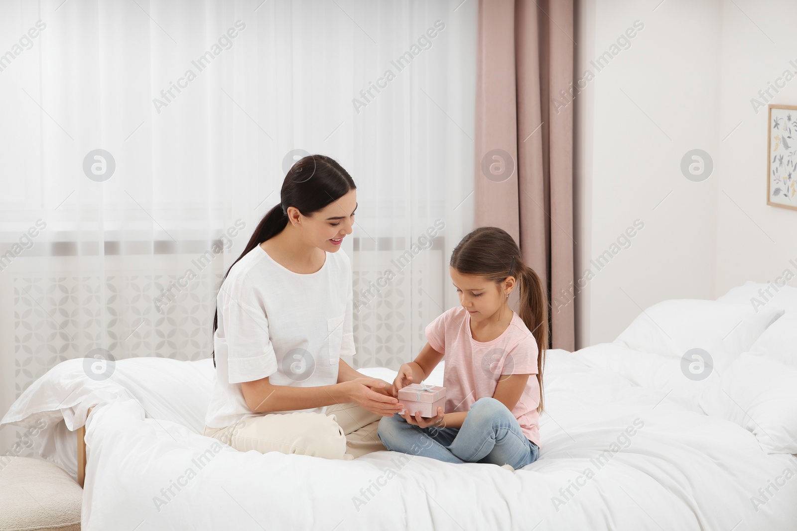 Photo of Daughter gifting happy woman gift box on bed at home. Mother's day celebration