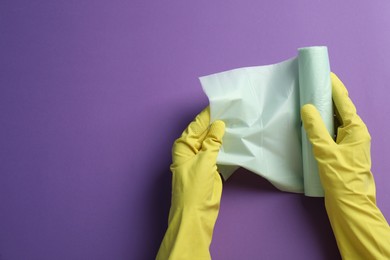 Janitor in rubber gloves holding roll of color garbage bags over purple background, top view. Space for text