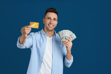 Happy man with cash money and credit card on blue background