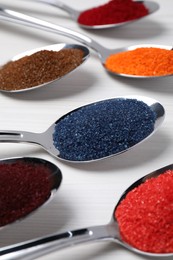 Spoons with different food coloring on white wooden table, closeup