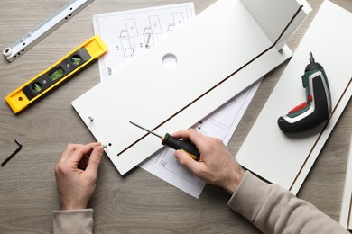 Photo of Man with screwdriver assembling white furniture at table, top view