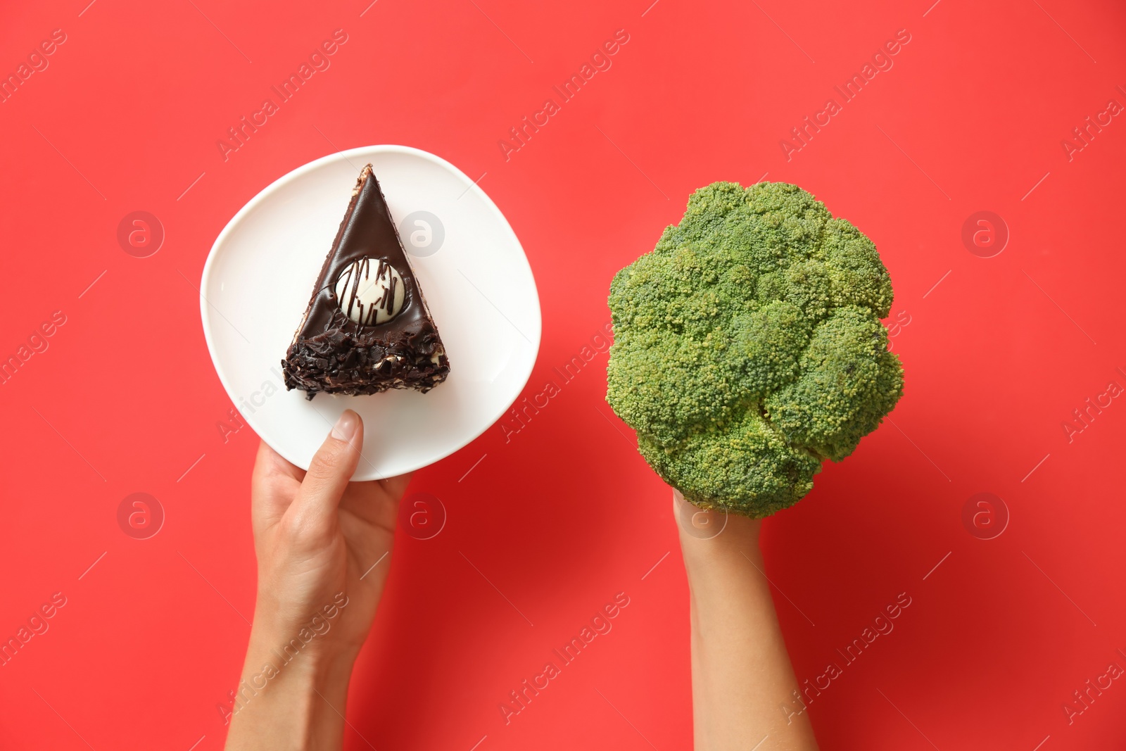 Photo of Top view of woman choosing between cake and healthy broccoli on red background, closeup