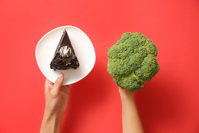 Photo of Top view of woman choosing between cake and healthy broccoli on red background, closeup