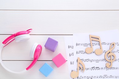 Notes, music sheets, headphones and cubes on white wooden table, flat lay with space for text. Baby song concept