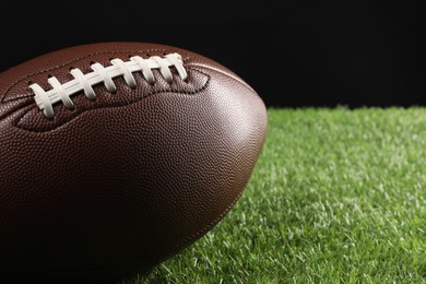 Photo of Leather American football ball on green grass against black background, closeup. Space for text