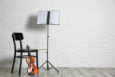 Photo of Violin, chair and note stand with music sheets near brick wall. Space for text