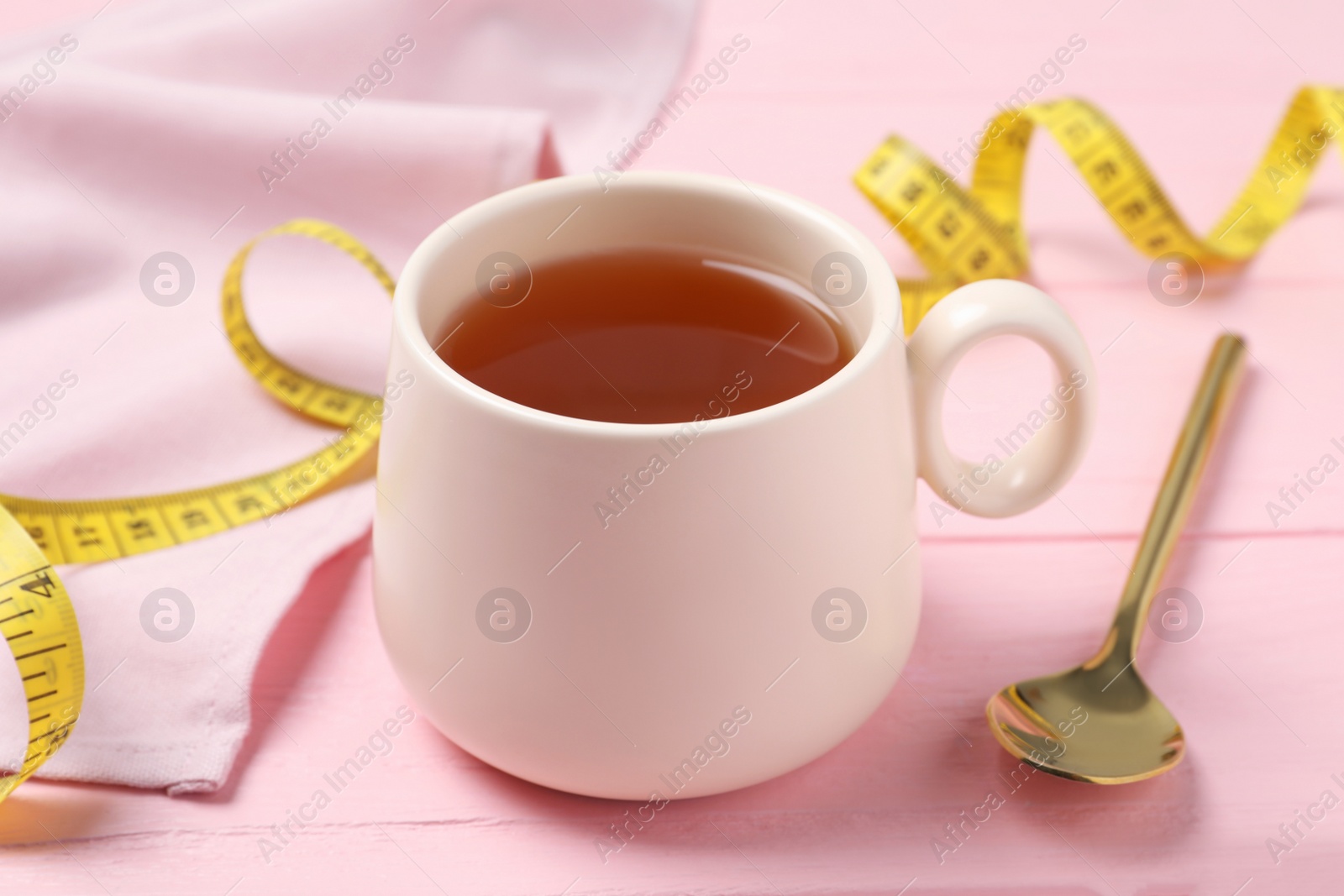 Photo of Cup of herbal diet tea, spoon and measuring tape on pink wooden table, closeup. Weight loss concept