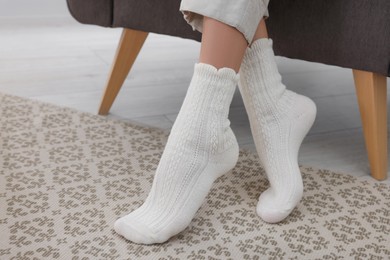 Photo of Woman wearing warm knitted socks at home, closeup. Space for text