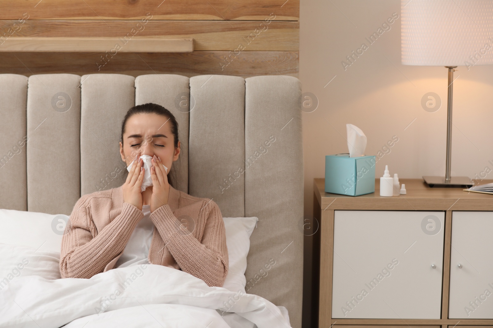 Photo of Sick young woman with napkins and nasal spray in bed at home