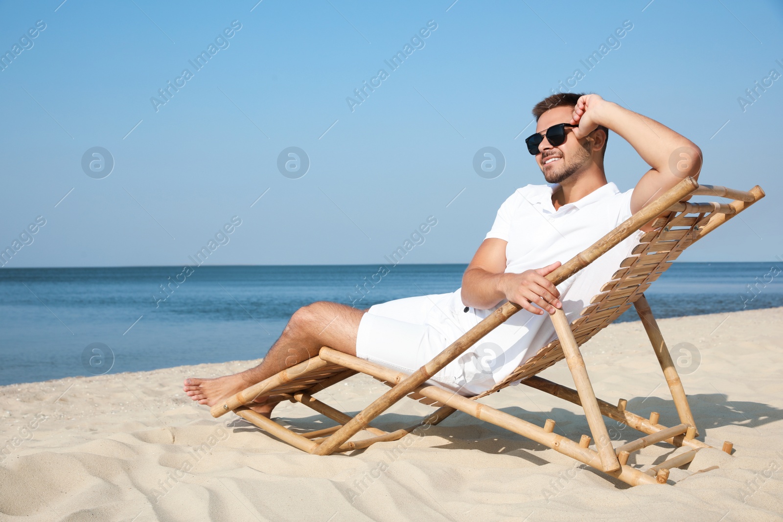 Photo of Young man relaxing in deck chair on sandy beach