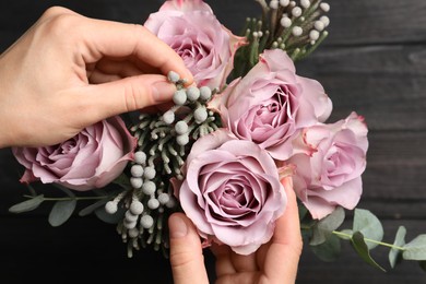 Florist creating beautiful bouquet at black wooden table, top view