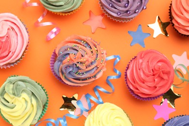 Photo of Delicious cupcakes with bright cream and party decor on orange background, flat lay