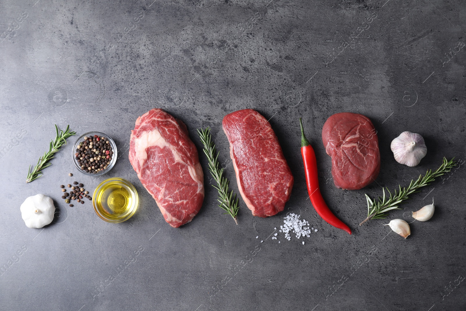 Photo of Raw beef steaks, oil and spices on grey table, flat lay