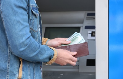 Man with money near cash machine outdoors, closeup