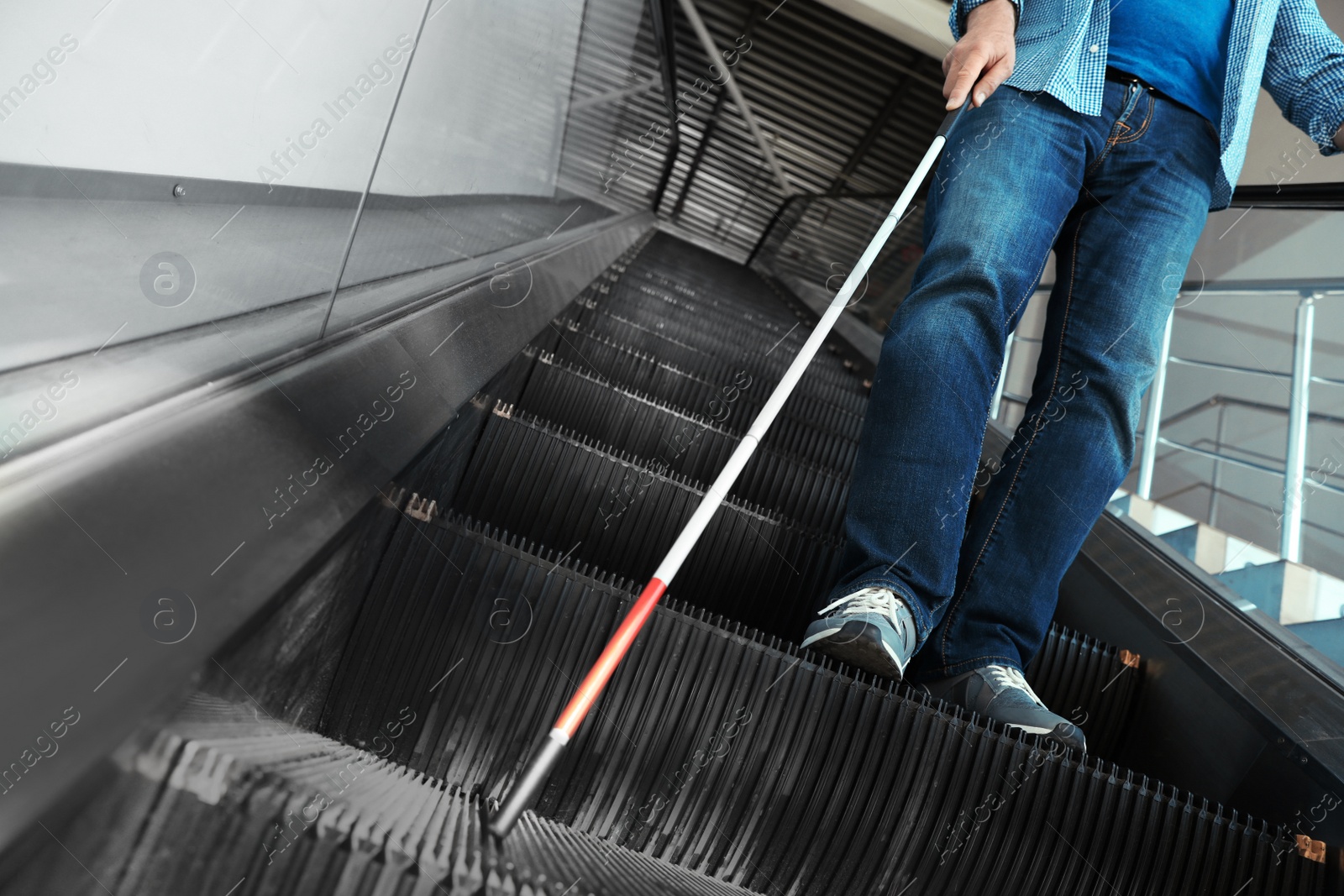 Photo of Blind person with long cane on escalator indoors