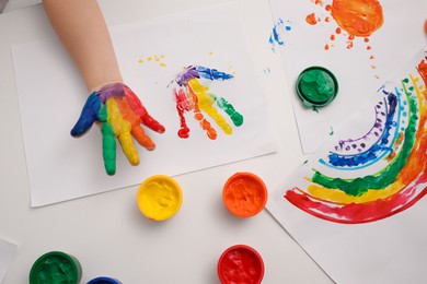 Photo of Little child making hand print on paper with painted palm at white table indoors, top view