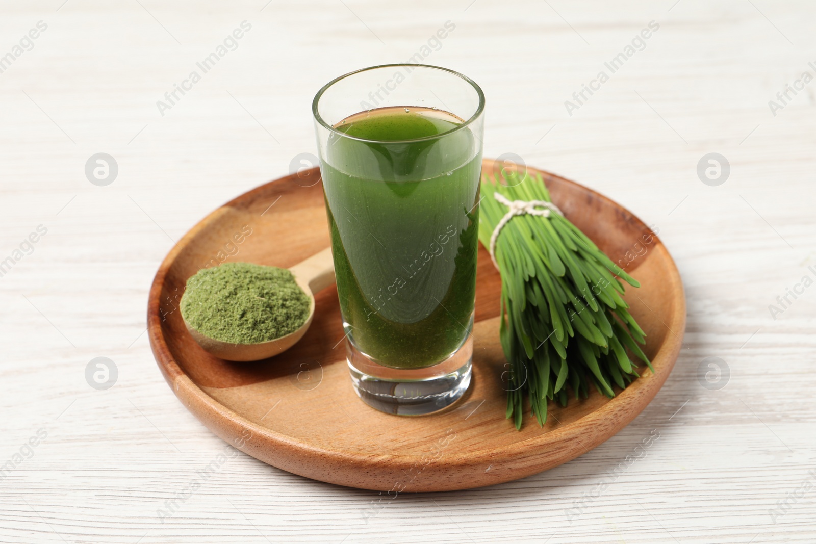Photo of Wheat grass drink in shot glass, spoon of green powder and fresh sprouts on white wooden table