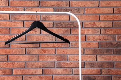 Photo of Black clothes hanger on rack near red brick wall. Space for text