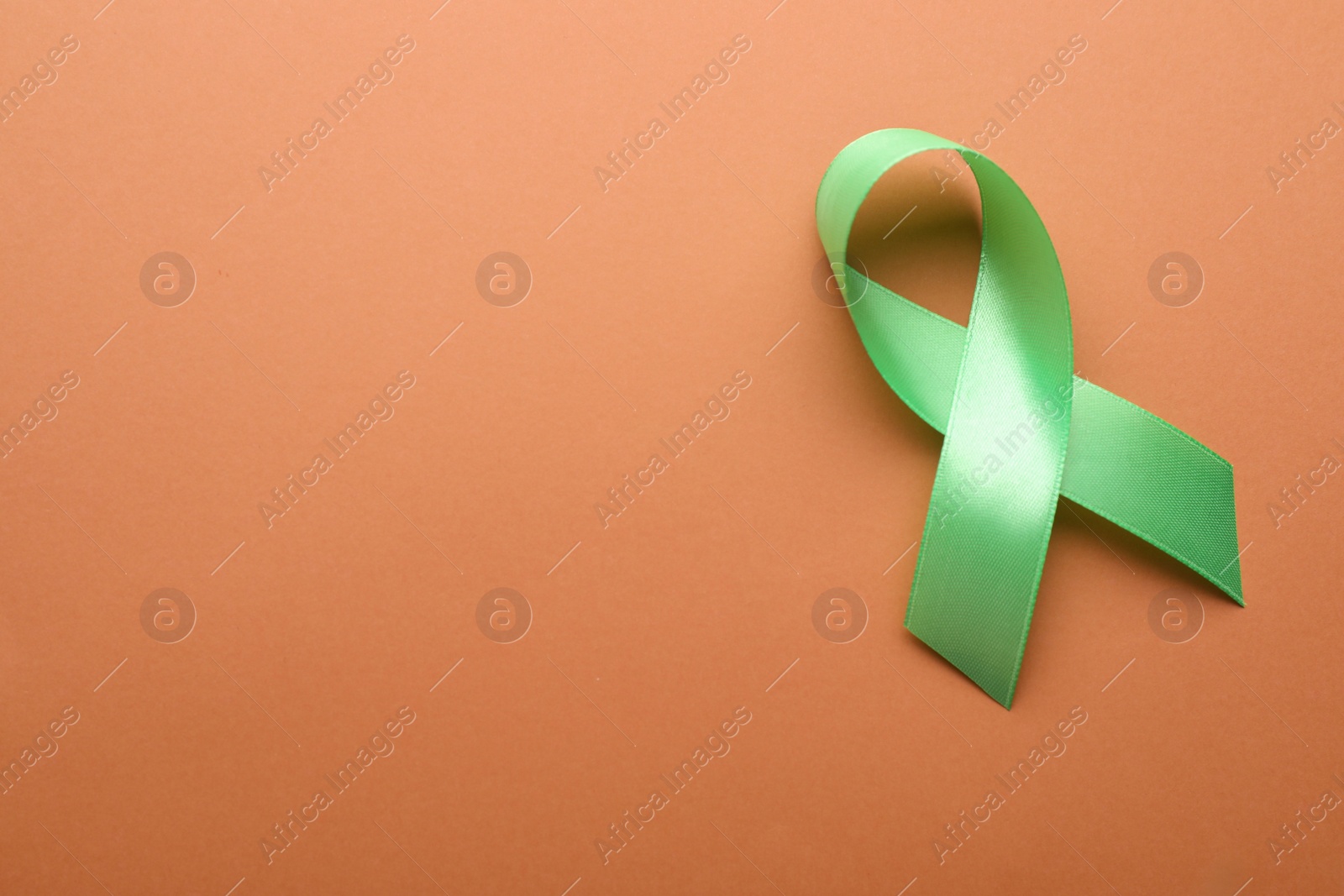 Photo of World Mental Health Day. Green ribbon on pale orange background, top view with space for text