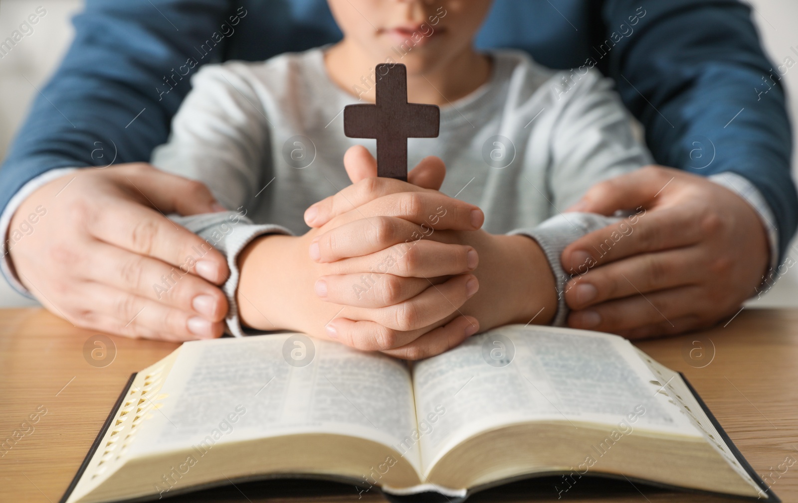 Photo of Boy and his godparent praying together at wooden table, closeup