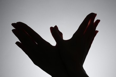 Photo of Shadow puppet. Woman making hand gesture like bird on grey background, closeup