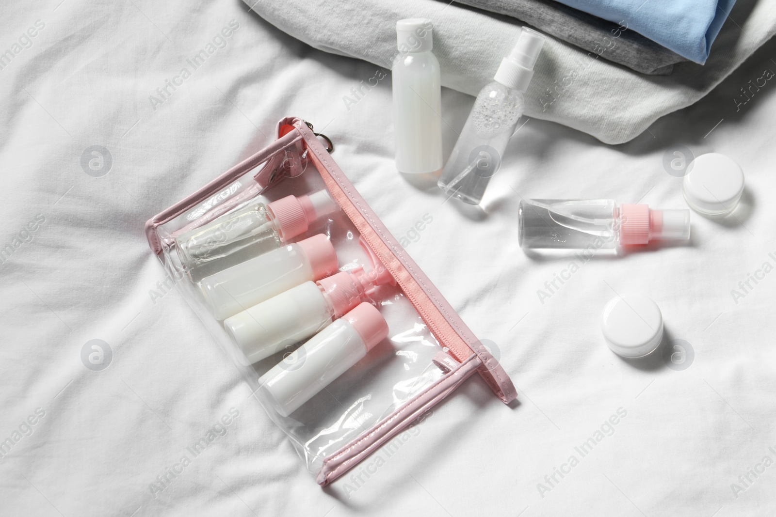 Photo of Cosmetic travel kit. Plastic bag with small containers of personal care products on bed, above view