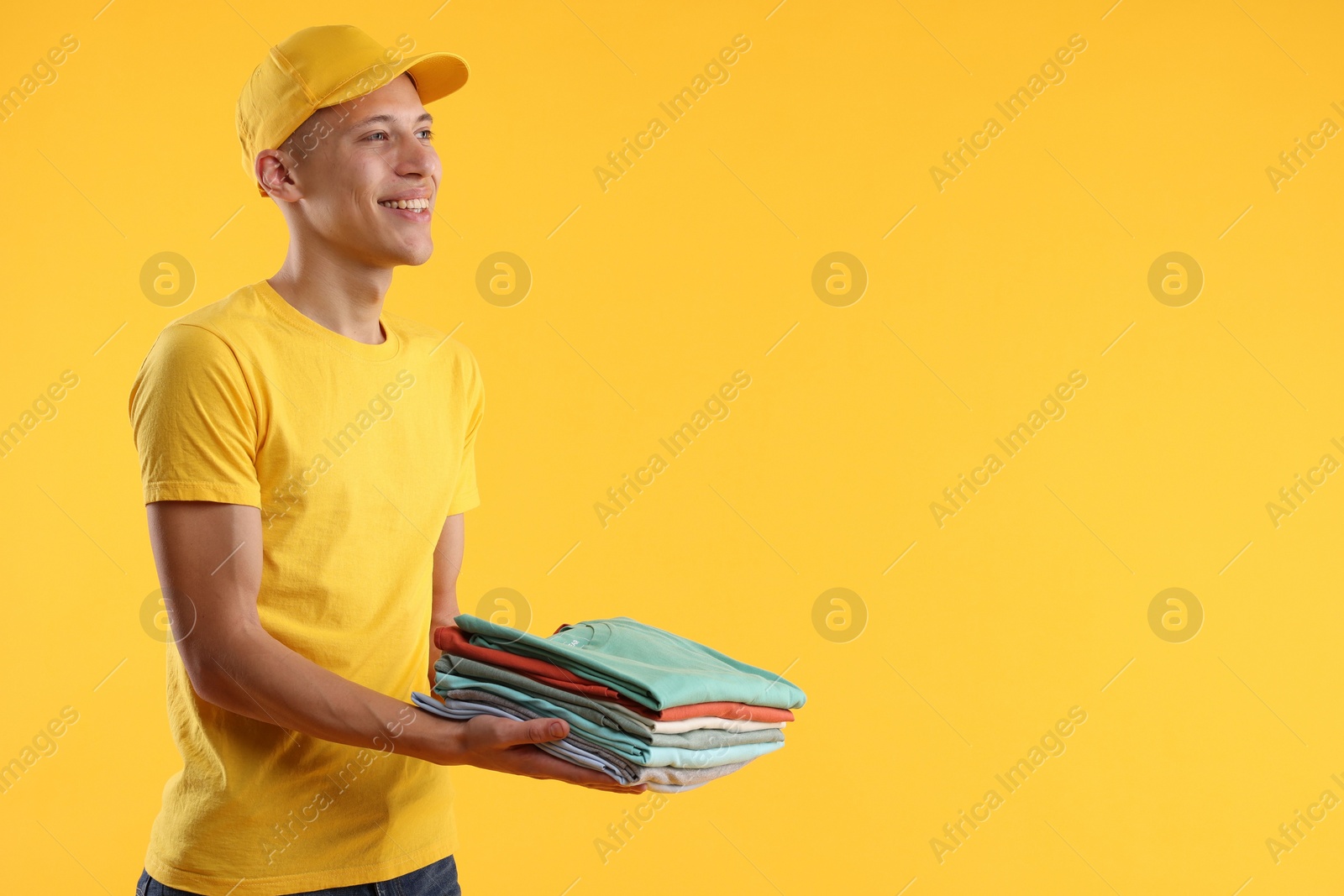 Photo of Dry-cleaning delivery. Happy courier holding folded clothes on orange background, space for text