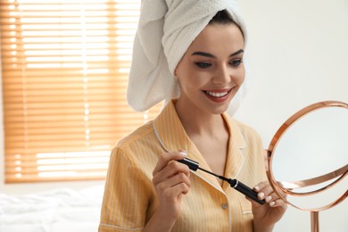 Beautiful woman with mirror applying makeup in bedroom