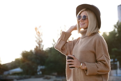 Woman in stylish sweater with cup of coffee on city street