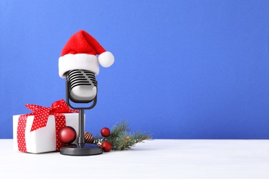 Photo of Retro microphone with Santa hat, gift box and festive decor on table against blue background, space for text. Christmas music