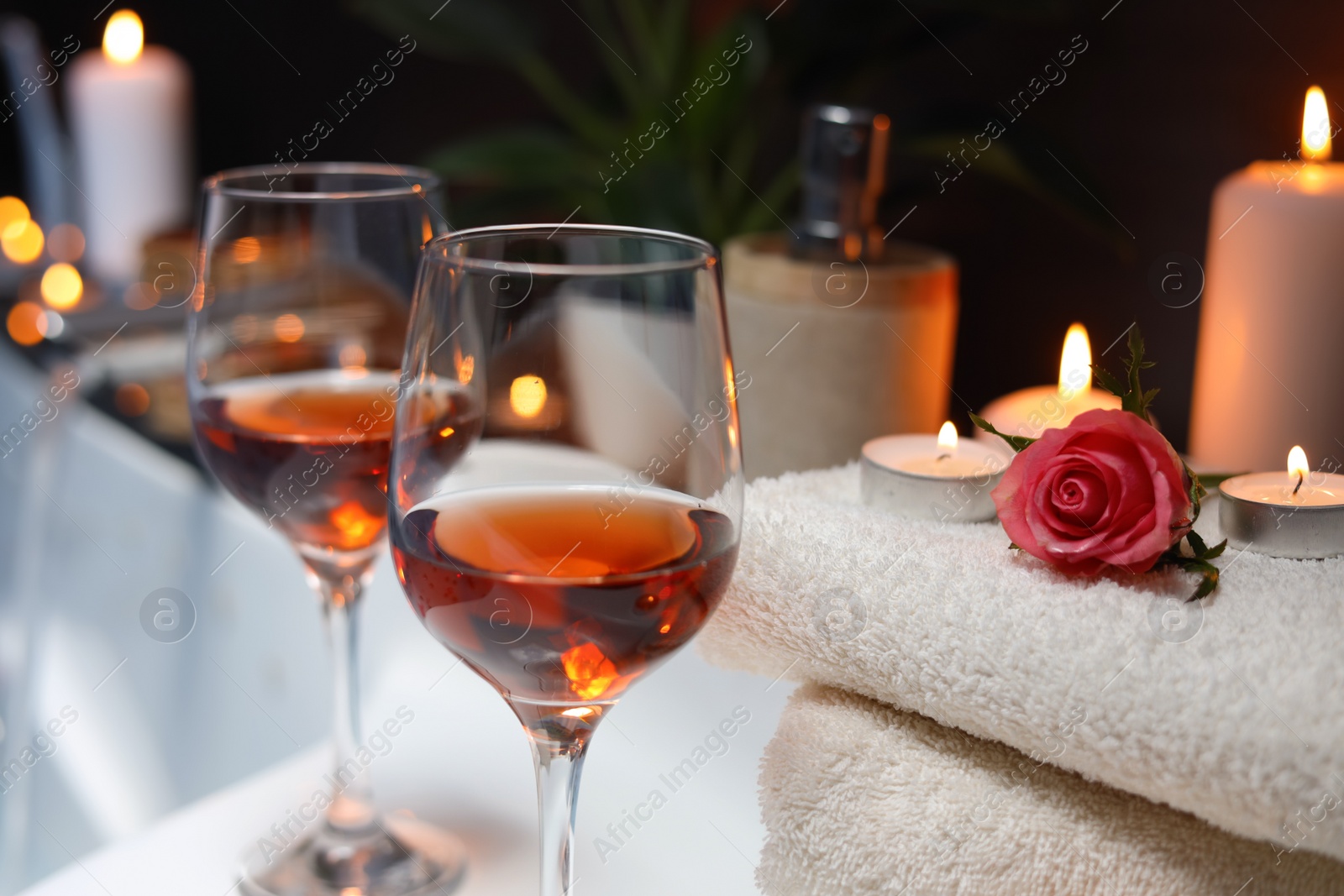 Photo of Wine in glasses and rose on edge of bath indoors, closeup. Romantic atmosphere