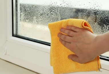 Photo of Woman wiping window glass with drops of condensate indoors, closeup. Space for text