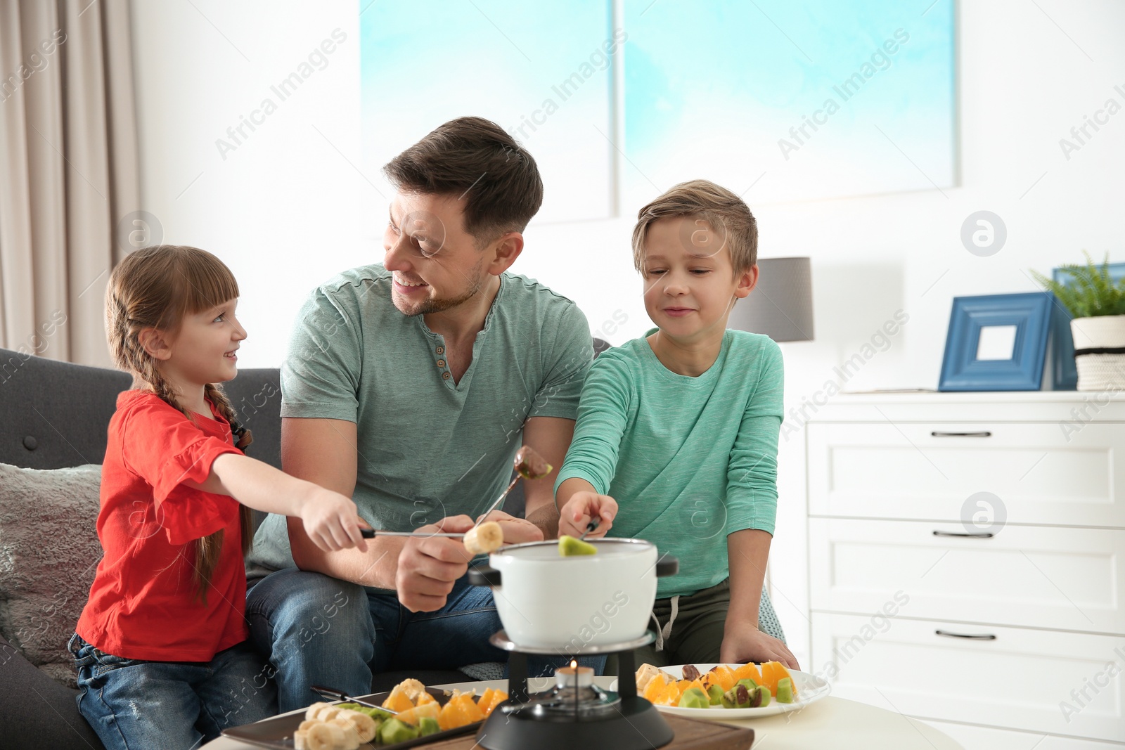 Photo of Children enjoying fondue dinner with father at home