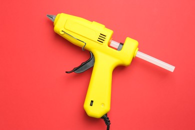 Photo of Yellow glue gun with stick on red background, top view