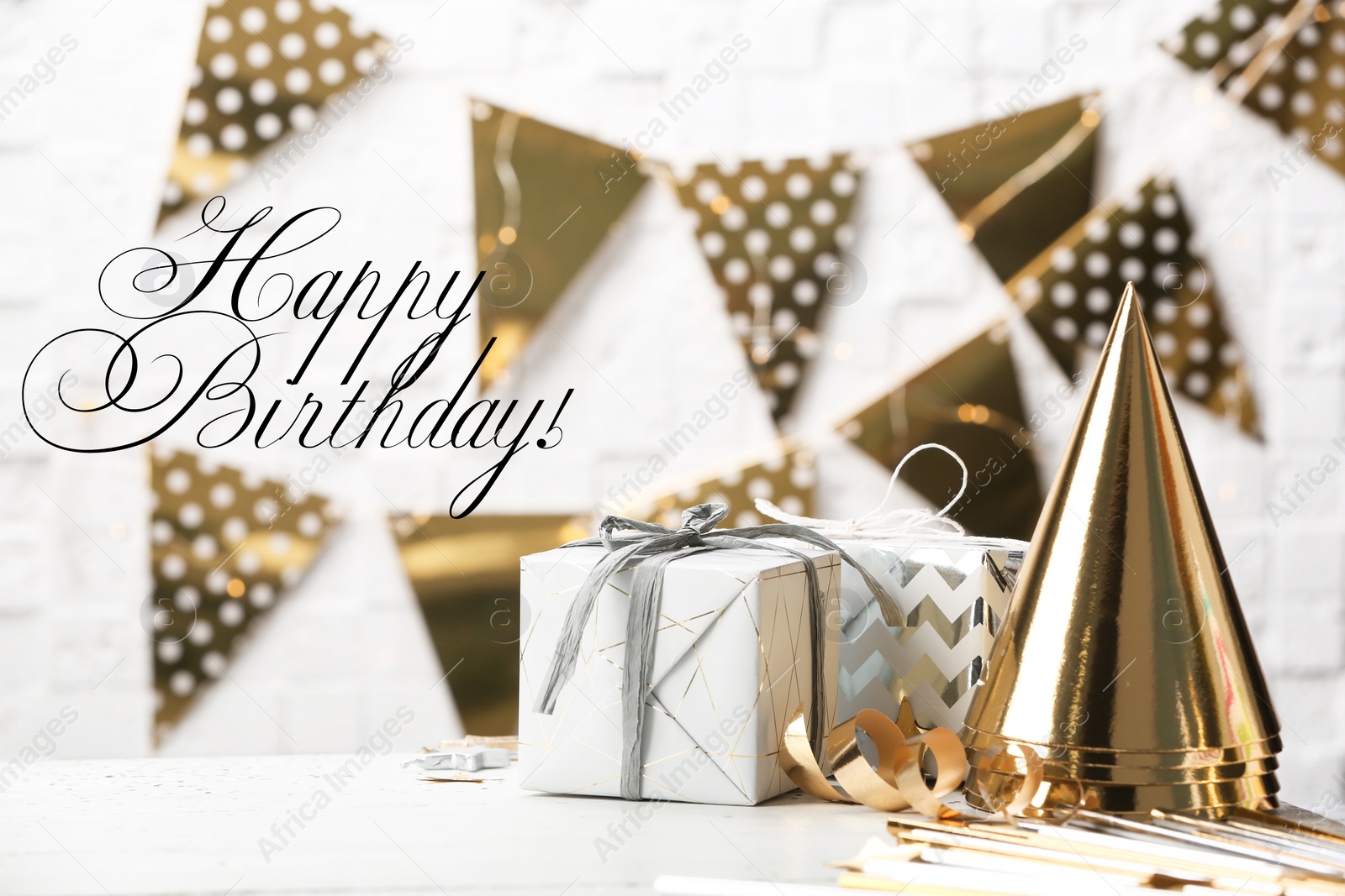 Photo of Gifts, party cones and greeting HAPPY BIRTHDAY on blurred background